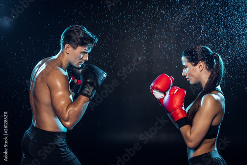 Side view of two boxers in boxing gloves training together under water drops on black © LIGHTFIELD STUDIOS