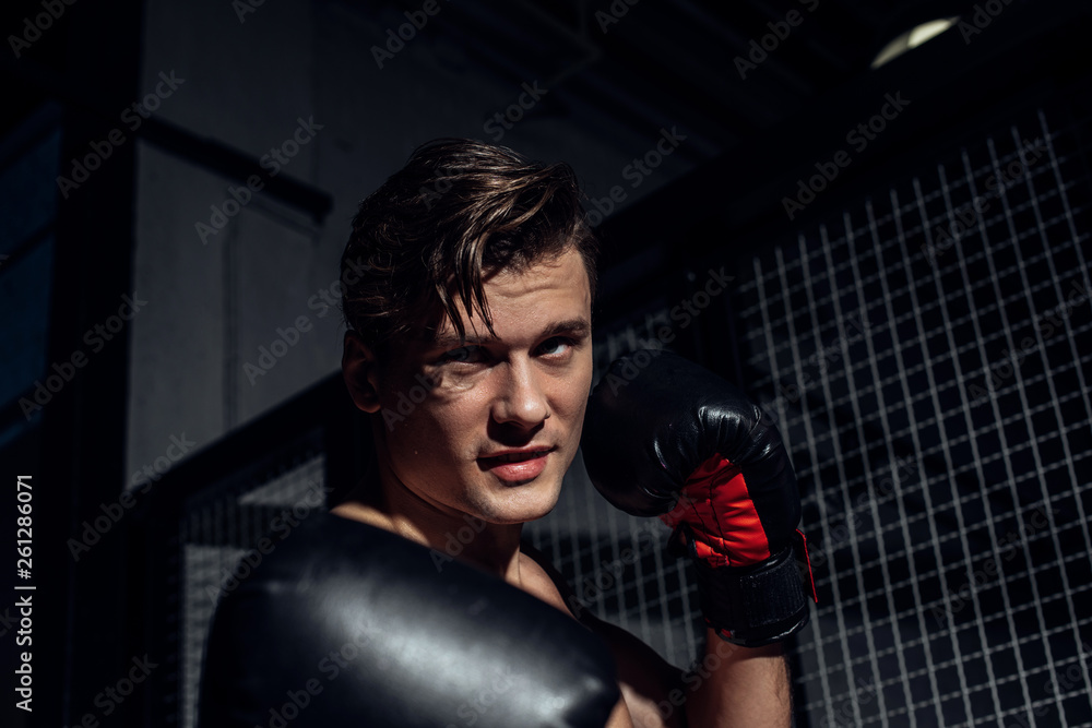Handsome boxer in black boxing gloves training and looking away