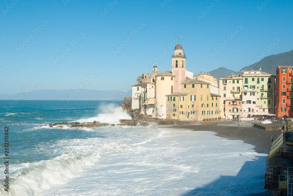 Church of Camogli in a day with sea storm that overwhelms beach and pier with blue sky