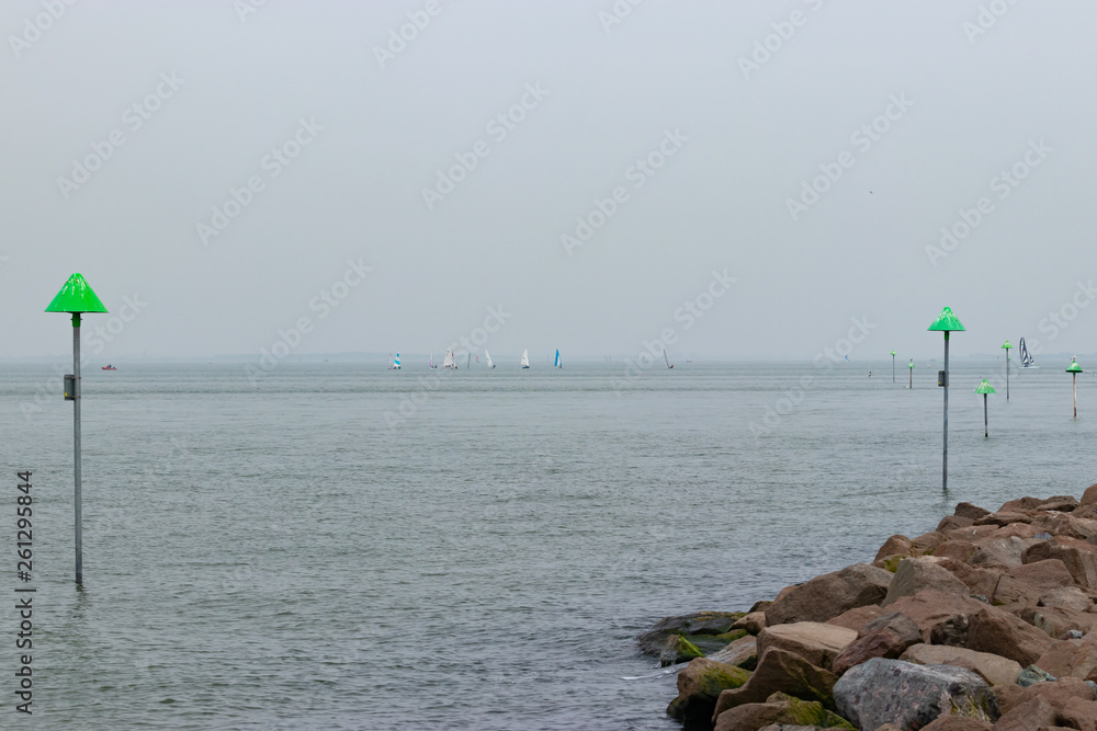 sailing boats on horizon and navigation markers with stones on foreground 