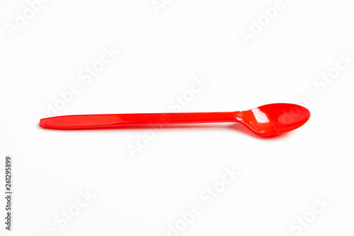 A single long and unused shiny red plastic spoon deliberately and artistically set on a plain white background.
