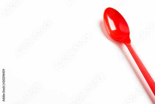 A single long and unused shiny red plastic spoon deliberately and artistically set on a plain white background.