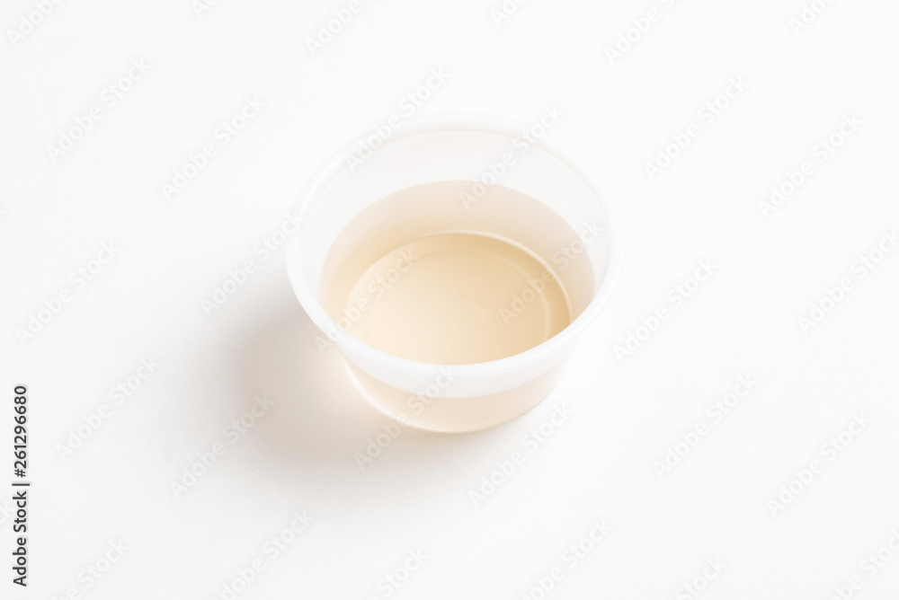 A fresh urine sample in a small round plastic cup container set on a plain white paper background. A fresh urine sample in a small round plastic cup container set on a plain white paper background.