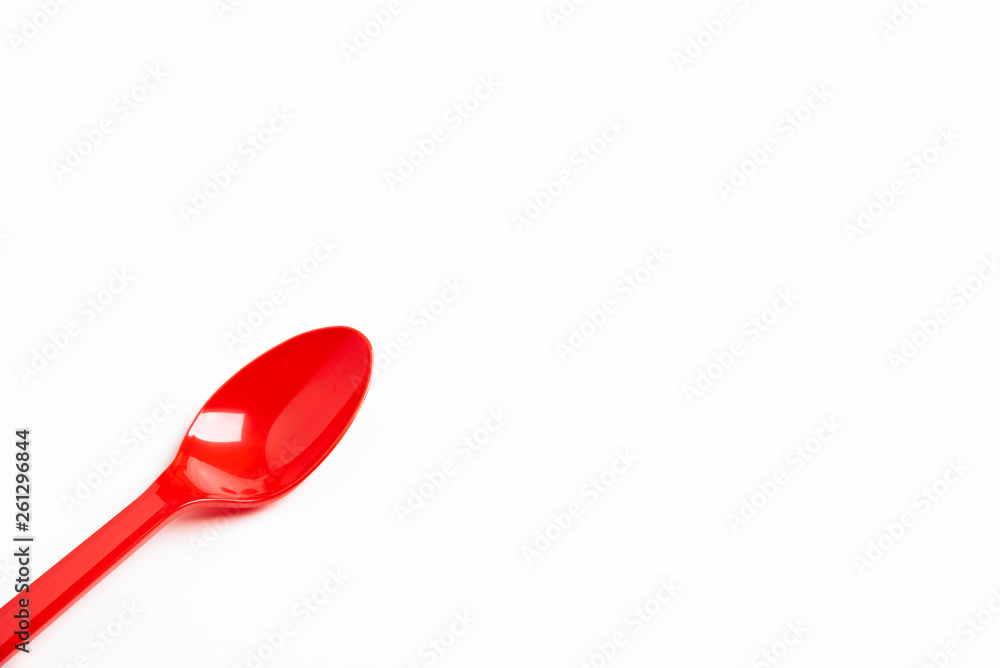 A single long and unused shiny red plastic spoon deliberately and artistically set on a plain white background. A single long and unused shiny red plastic spoon deliberately and artistically set on a plain white background.