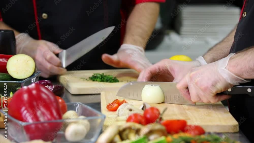A chef in the kitchen cutting the onion and greenery for a serving