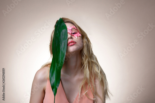 Blonde-haired model holding big green leaf near her face