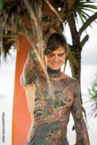 Photography Attractive male surfer in tattoos on the ocean with an orange bright longboard surfboard
