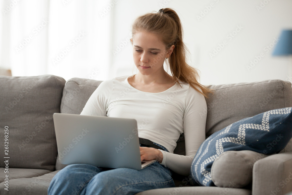 Serious woman working, using laptop, typing, sitting alone on sofa Serious woman working, using laptop, typing, sitting alone on sofa