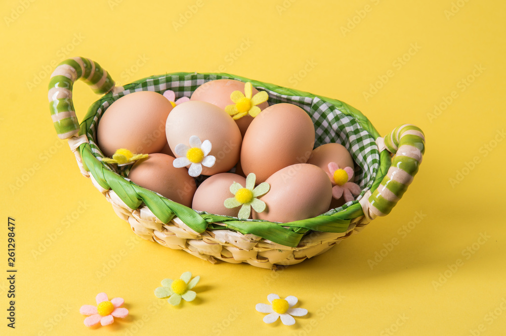 Close up. Easter still life. Rustic brown eggs in a wicker basket lined with checkered fabric. The decor of the felt flowers. Yellow background.