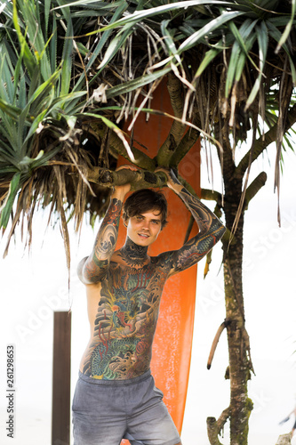 Photography Attractive male surfer in tattoos on the ocean with an orange bright longboard surfboard