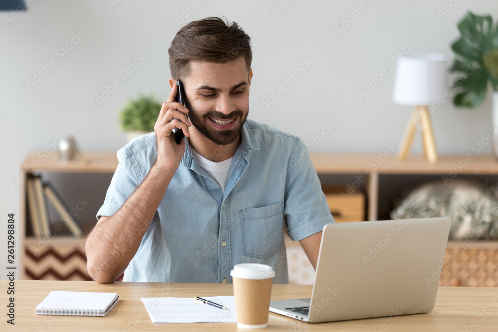 Smiling satisfied man talking on phone and using laptop at workplace Smiling satisfied man talking on phone and using laptop at workplace