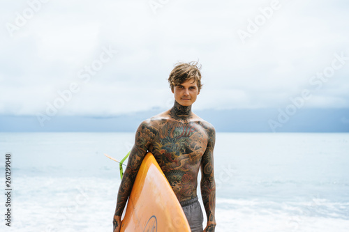 Canvas Print Attractive male surfer in tattoos on the ocean with an orange bright longboard surfboard