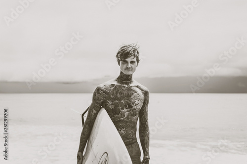 Canvas Print Attractive male surfer in tattoos on the ocean with an orange bright longboard surfboard