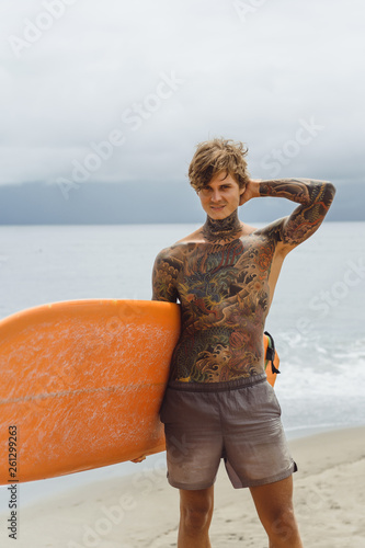 Photography Attractive male surfer in tattoos on the ocean with an orange bright longboard surfboard