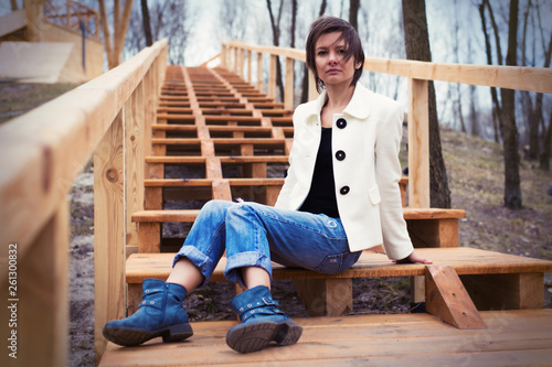 A girl in a white jacket sits on wooden steps in the park. © Konstiantyn Zapylaie