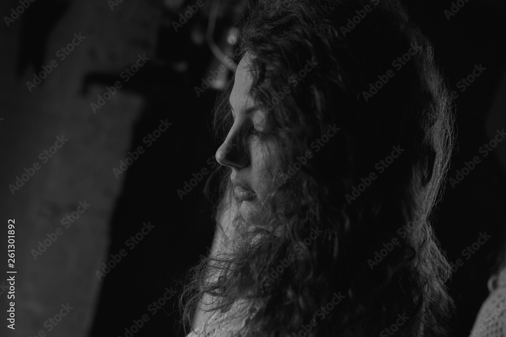 Authentic black and white horizontal portrait of young woman profile, standing in dark room. Close up detailed shot of curly haired sensual Caucasian female, posing indoors. Youth and beauty concept. Authentic black and white horizontal portrait of young woman profile, standing in dark room. Close up detailed shot of curly haired sensual Caucasian female, posing indoors. Youth and beauty concept.