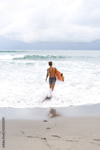Photography Attractive male surfer in tattoos on the ocean with an orange bright longboard surfboard