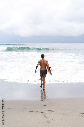 Canvas Print Attractive male surfer in tattoos on the ocean with an orange bright longboard surfboard