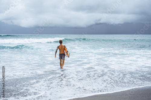 Photography Attractive male surfer in tattoos on the ocean with an orange bright longboard surfboard