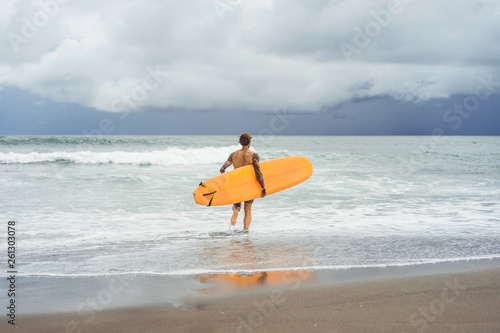 Photography Attractive male surfer in tattoos on the ocean with an orange bright longboard surfboard
