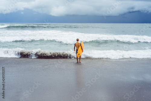 Photography Attractive male surfer in tattoos on the ocean with an orange bright longboard surfboard