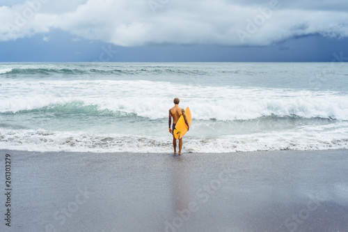 Photography Attractive male surfer in tattoos on the ocean with an orange bright longboard surfboard