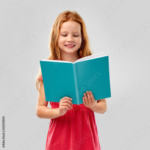 childhood and people concept - smiling red haired girl reading book over grey background © Syda Productions