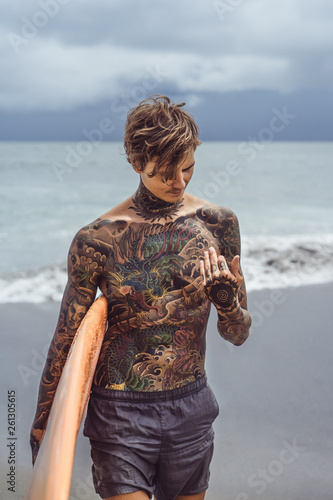 Canvas Print Attractive male surfer in tattoos on the ocean with an orange bright longboard surfboard