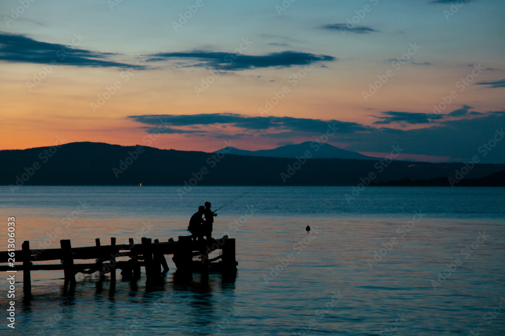 Pesca rilassante su un pontile sul lago calmo al tramonto