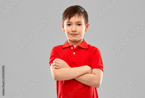 childhood, expressions and people concept - smiling little boy in red polo t-shirt with crossed arms over grey background