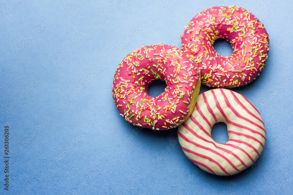 Creative layout made of pink glazed donuts. Flat lay. Food concept. Macro concept. Various decorated doughnuts on blue background. Sweet and colourful doughnuts Creative layout made of pink glazed donuts. Flat lay. Food concept. Macro concept. Various decorated doughnuts on blue background. Sweet and colourful doughnuts