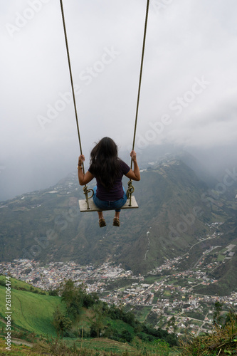 Beautiful young woman on the swing. Swinging over beautiful mountain. Banos, Ecuador.