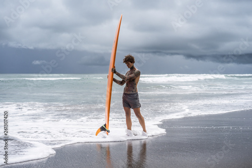 Canvas Print Attractive male surfer in tattoos on the ocean with an orange bright longboard surfboard