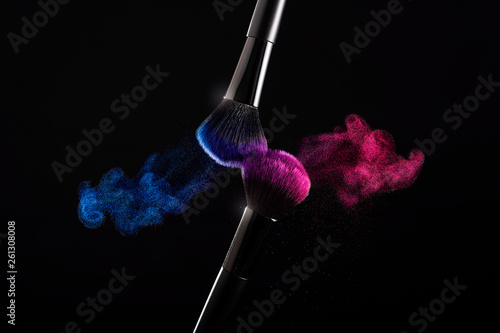 Cosmetic shades of different colors, red and blue, fly away from two make-up brushes creating a fancy pattern on a black background.