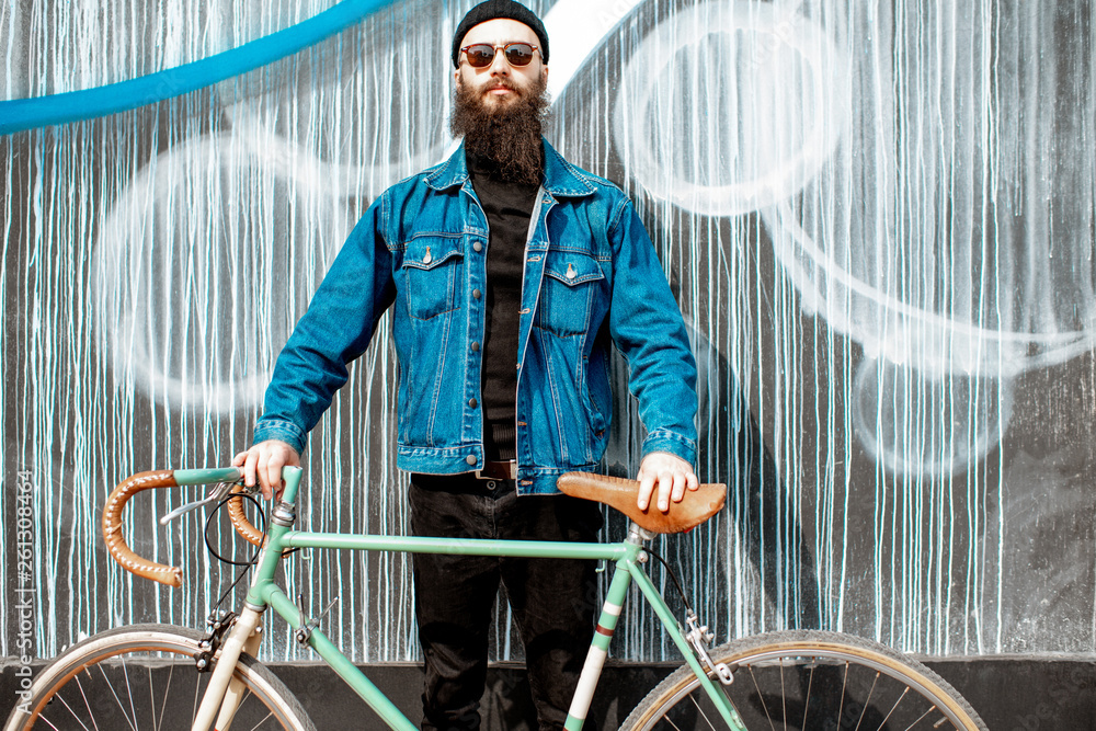 Portrait of a stylish bearded man dressed in jacket and hat with retro bicycle on the colorful wall background