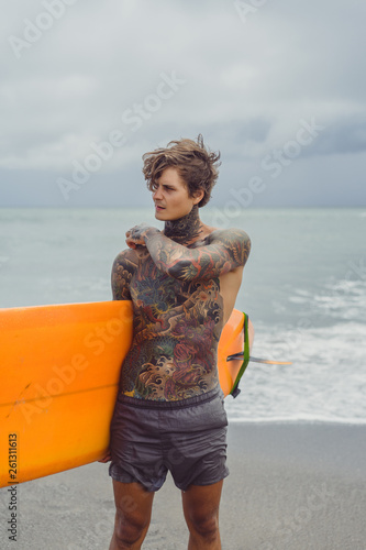 Photography Attractive male surfer in tattoos on the ocean with an orange bright longboard surfboard