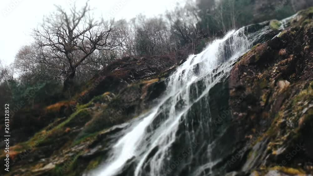 Low angle shot of a splashing waterfall, autumn colours and vibes with mossy rocks, and bold trees in Wicklow Mountains, Ireland Low angle shot of a splashing waterfall, autumn colours and vibes with mossy rocks, and bold trees in Wicklow Mountains, Ireland