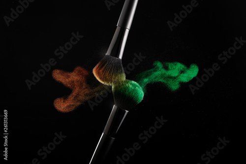 cosmetic shades of different colors, red and green, fly away from two makeup brushes creating a fancy pattern on a black background.