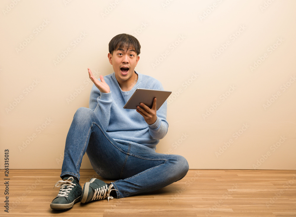 Young chinese man sitting using his tablet surprised and shocked Young chinese man sitting using his tablet surprised and shocked