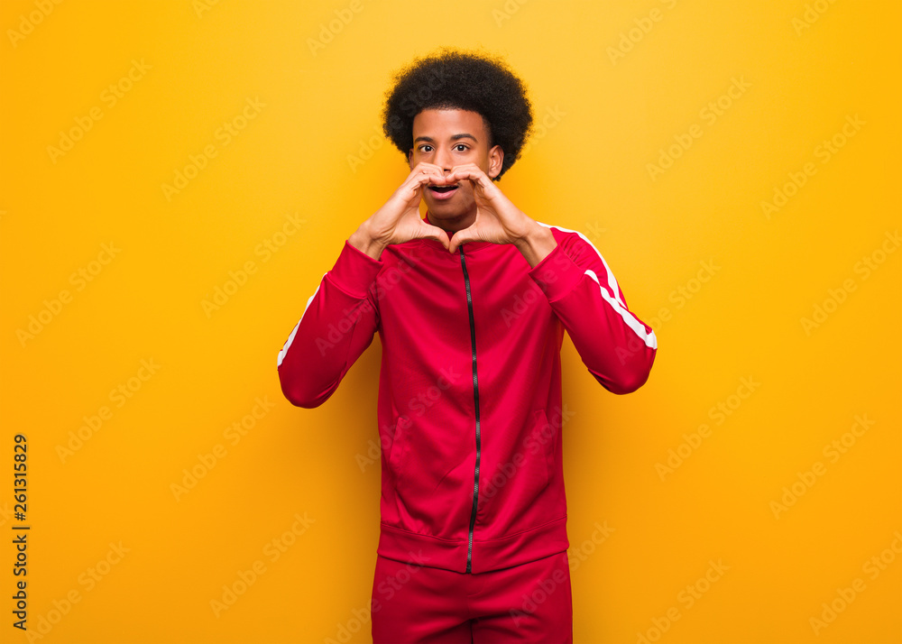 Young sport black man over an orange wall doing a heart shape with hands