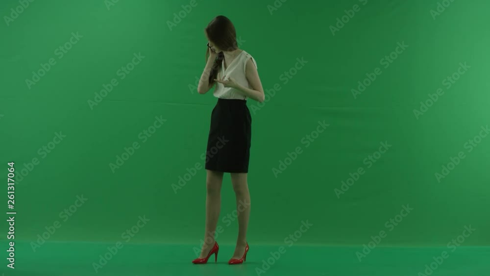 beautiful shouting young business woman in white shirt and black skirt is talking on her mobile phone standing sideways against green screen. beautiful shouting young business woman in white shirt and black skirt is talking on her mobile phone standing sideways against green screen.