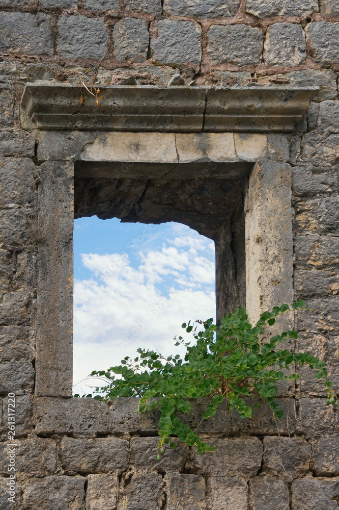 Wall of an old destroyed building with a window through which a blue sky with white clouds is visible