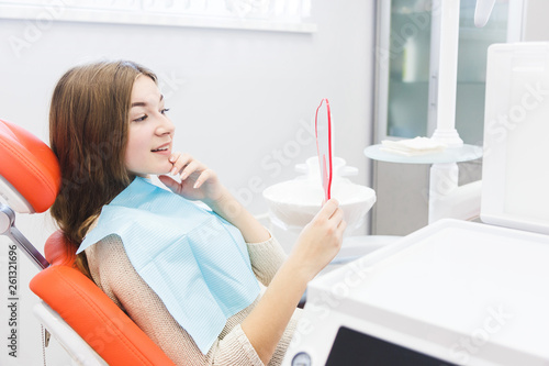 Dental clinic. Reception, examination of the patient. Teeth care. Young girl smiling, looking in the mirror after a dental checkup at her dentist