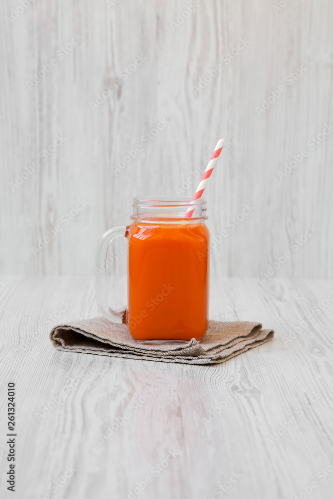 Carrot smoothie in a glass jar on a white wooden background, side view.