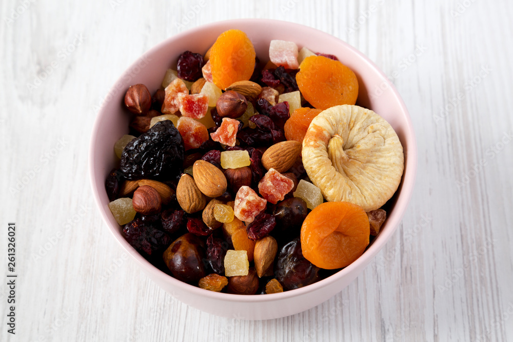 Dried fruits and nuts in a pink bowl over white wooden surface, low angle view. Dried fruits and nuts in a pink bowl over white wooden surface, low angle view.