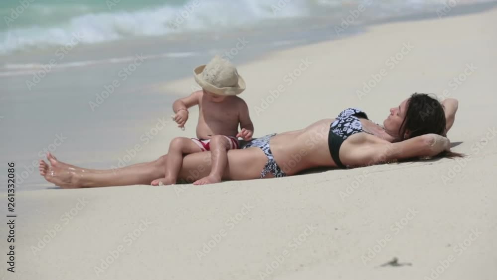 Mom and toddler boy, playing together on the beach edge, water splashing them Mom and toddler boy, playing together on the beach edge, water splashing them
