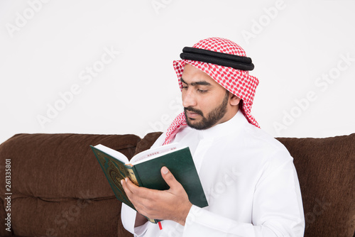 Arab Muslim man sitting on sofa chair and reading the holy Quran