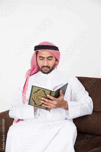 Arab Muslim man sitting on sofa chair and reading the holy Quran