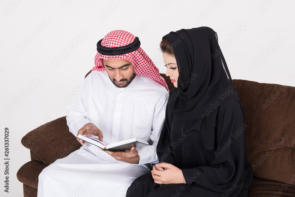 Arab man reading from the Holy Quran for his wife while sitting at home on sofa chair Arab man reading from the Holy Quran for his wife while sitting at home on sofa chair