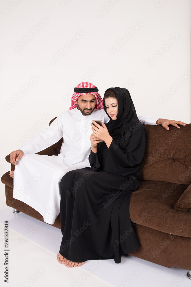 Arab muslim married couple using smart phone while sitting on sofa chair at home Arab muslim married couple using smart phone while sitting on sofa chair at home